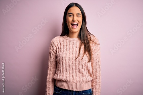 Young beautiful brunette woman wearing casual sweater over isolated pink background winking looking at the camera with sexy expression, cheerful and happy face. © Krakenimages.com