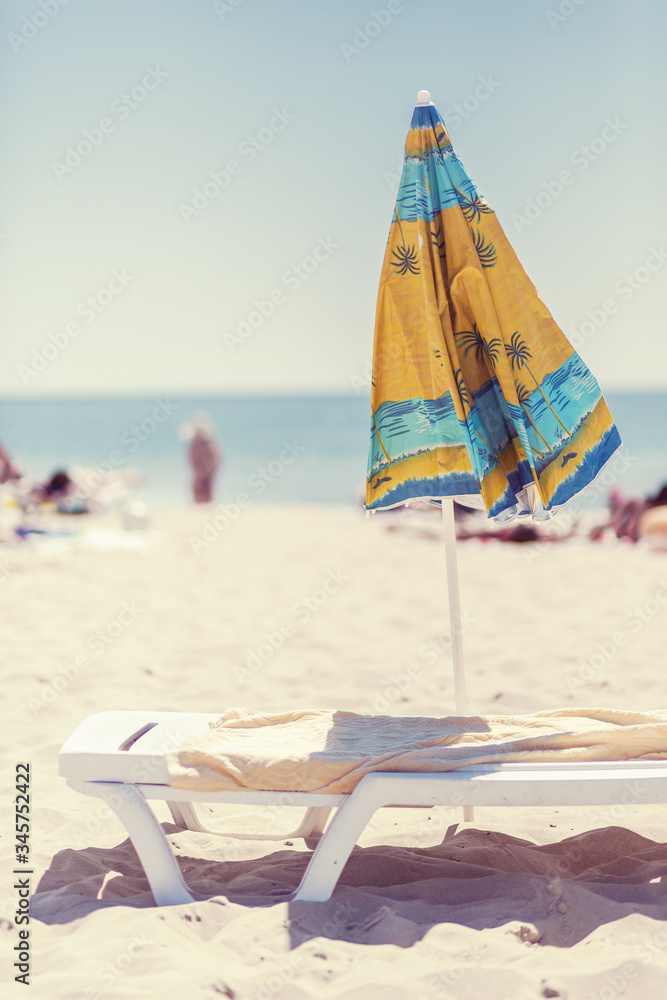 Summer vertical composition of a beach umbrella and deck chair with a carelessly thrown beach towel. Sun sand sea and beach Summer vertical composition of a beach umbrella and deck chair with a carelessly thrown beach towel. Sun sand sea and beach