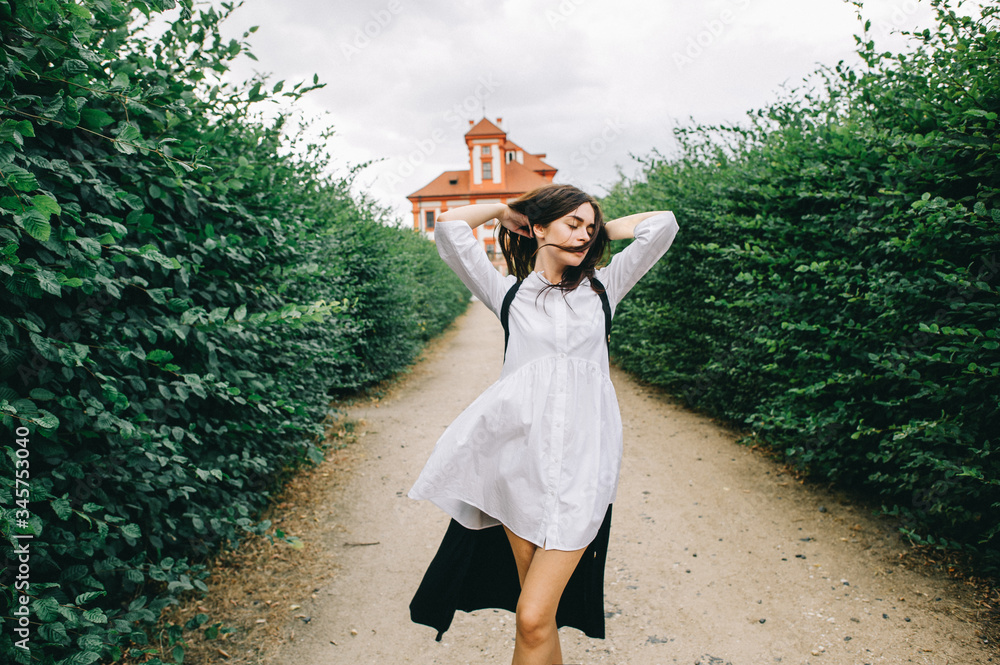 A young caucasian stylish girl walking along the green alley on a red palace background