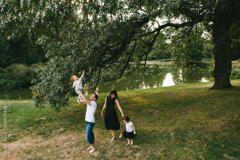 Handsome young father and beautiful mother in sunny summer nature playing with their cute small childrens Handsome young father and beautiful mother in sunny summer nature playing with their cute small childrens