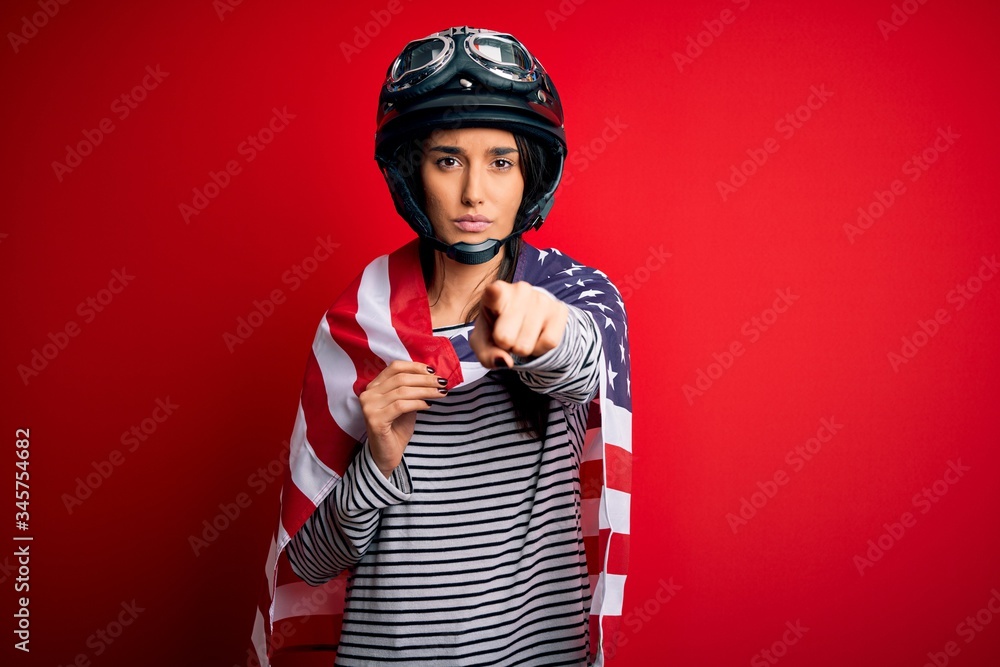 Young beautiful patriotic motorcyclist woman wearing moto helmet and united states flag pointing with finger to the camera and to you, hand sign, positive and confident gesture from the front Young beautiful patriotic motorcyclist woman wearing moto helmet and united states flag pointing with finger to the camera and to you, hand sign, positive and confident gesture from the front