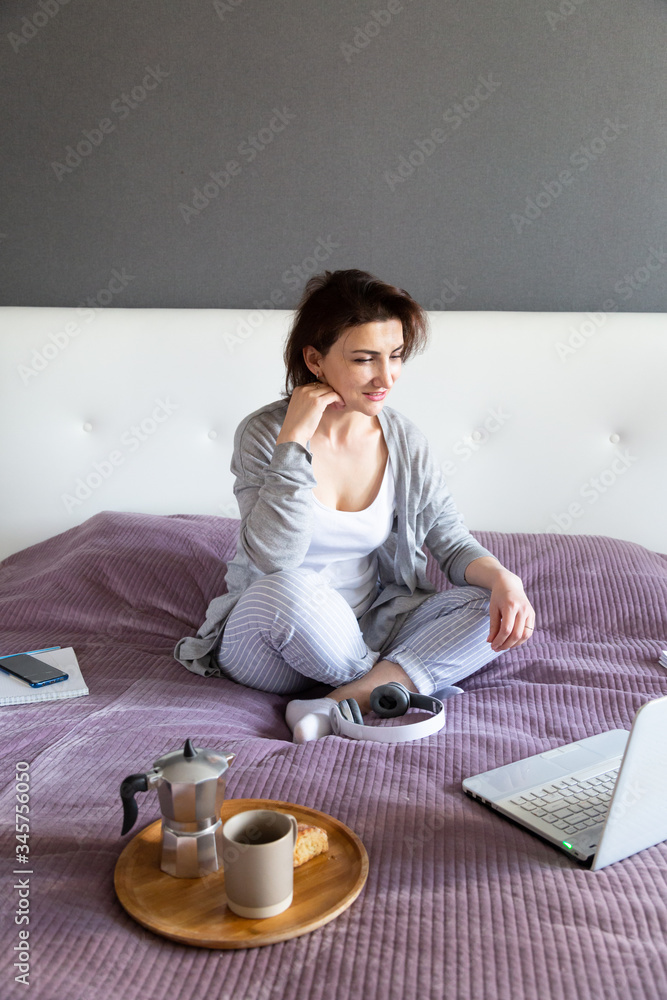 Young woman in grey working at home in her bedroom, freelance work with laptop.