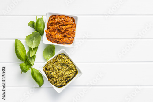 Green basil and red tomato pesto dip sauce and basil leaves.