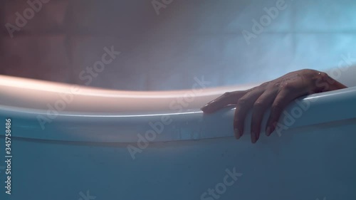 A woman is touching the edge of the white bathtub elegantly