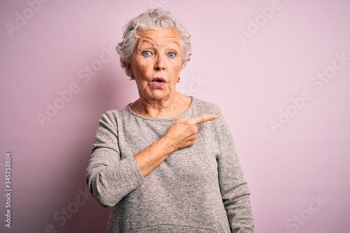 Senior beautiful woman wearing casual t-shirt standing over isolated pink background Surprised pointing with finger to the side, open mouth amazed expression.