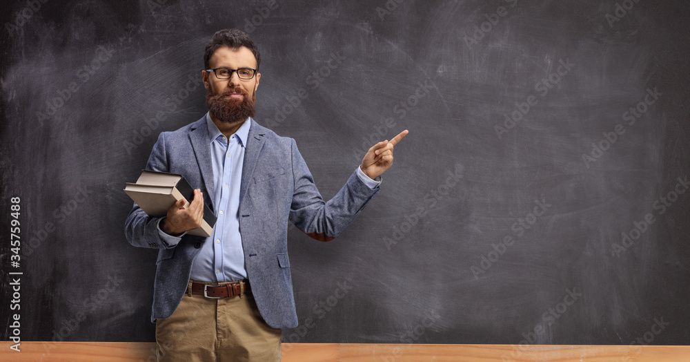 Male teacher holding books and pointing at a chalkboard