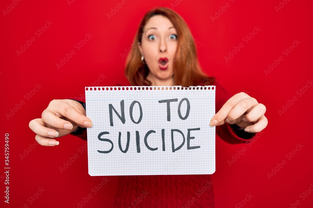 Beautiful redhead woman holding banner showing no to suicide message over red background scared in shock with a surprise face, afraid and excited with fear expression Beautiful redhead woman holding banner showing no to suicide message over red background scared in shock with a surprise face, afraid and excited with fear expression