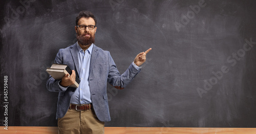 Obraz na plátně Male teacher holding books and pointing at a chalkboard