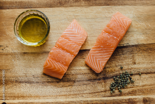 Two pieces of raw salmon, a bowl of olive oil  and a handful of black pepper on wooden table, top view. Ingredients for dinner or for sushi. Healthy fats, good fats concept