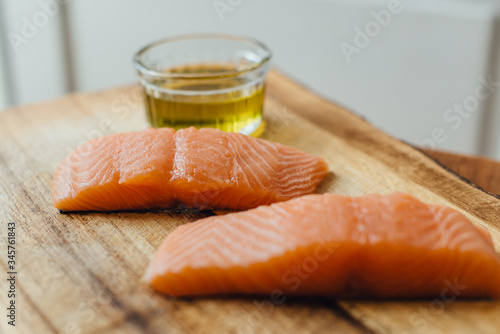 Two pieces of raw salmon, a bowl of olive oil on a wooden table. Ingredients for dinner or for sushi. Healthy fats, good fats concept.