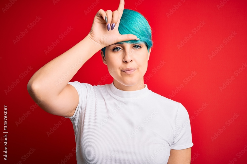 Young beautiful woman with blue fashion hair wearing casual t-shirt over red background making fun of people with fingers on forehead doing loser gesture mocking and insulting. Young beautiful woman with blue fashion hair wearing casual t-shirt over red background making fun of people with fingers on forehead doing loser gesture mocking and insulting.