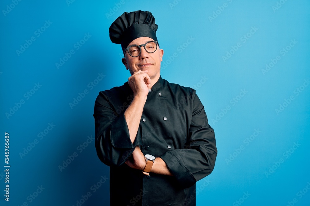 Middle age handsome grey-haired chef man wearing cooker uniform and hat looking confident at the camera smiling with crossed arms and hand raised on chin. Thinking positive. Middle age handsome grey-haired chef man wearing cooker uniform and hat looking confident at the camera smiling with crossed arms and hand raised on chin. Thinking positive.