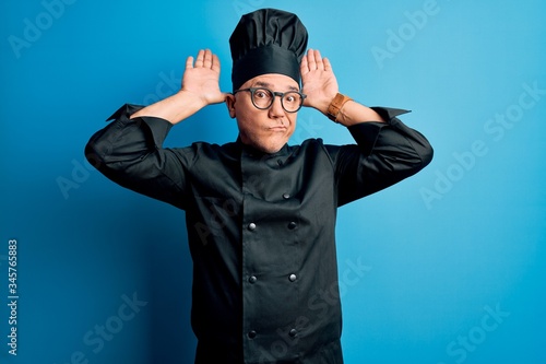 Middle age handsome grey-haired chef man wearing cooker uniform and hat Doing bunny ears gesture with hands palms looking cynical and skeptical. Easter rabbit concept.