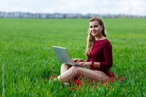 Young successful woman is sitting on green grass with a laptop in her hands. Work on the nature. Student girl working in a secluded place. New business ideas
