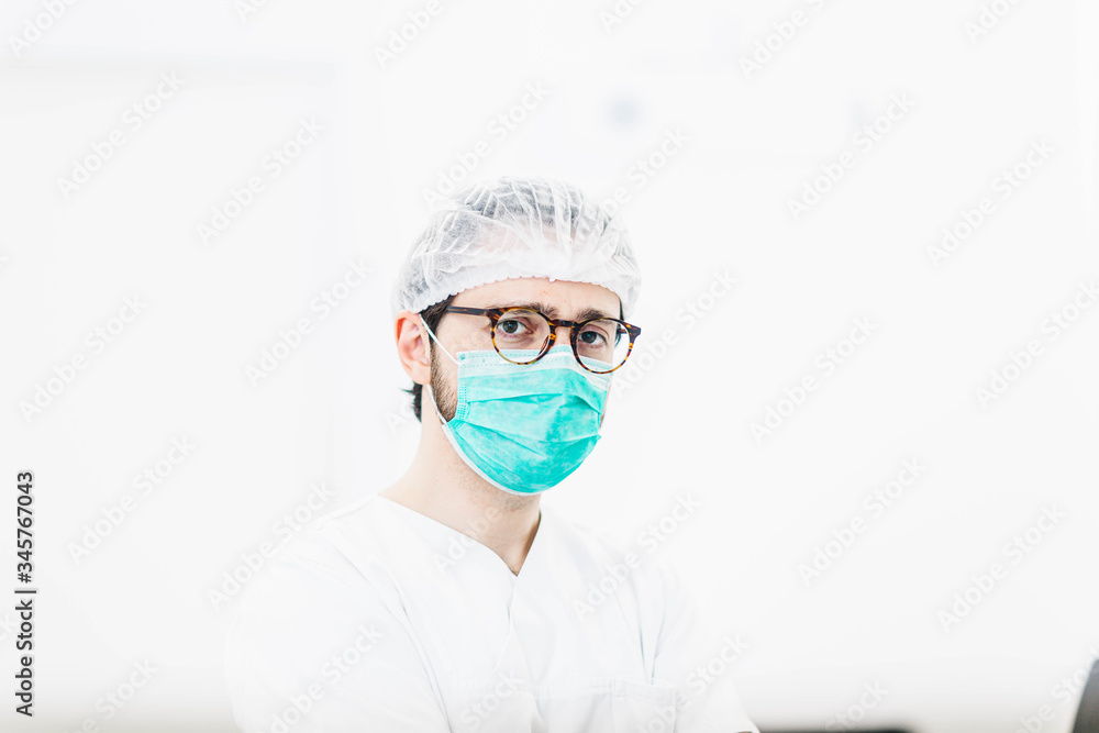Naklejka premium male surgeon doctor in uniform and medical mask stands in a bright clinic office.