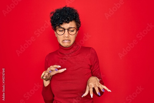 Young beautiful african american afro woman wearing turtleneck sweater and glasses disgusted expression, displeased and fearful doing disgust face because aversion reaction.