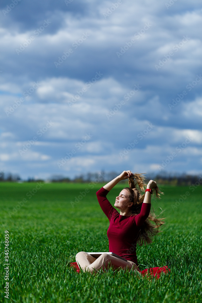 Young successful woman is sitting on green grass with a laptop in her hands. Rest after a good working day. Work on the nature. Student girl working in a secluded place. Workplace in nature Young successful woman is sitting on green grass with a laptop in her hands. Rest after a good working day. Work on the nature. Student girl working in a secluded place. Workplace in nature