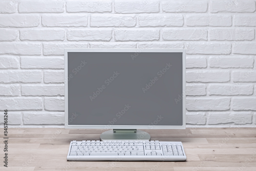 Fototapeta premium Blank screen computer monitor on working desk with brick wall