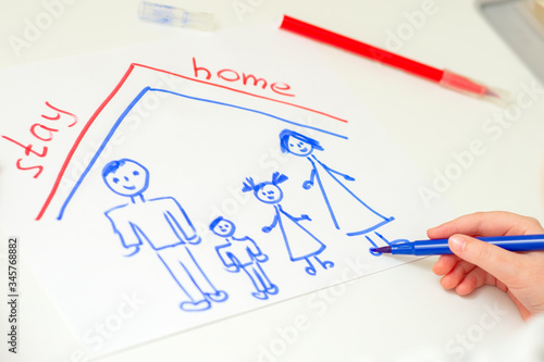 Child is drawing happy family with words Stay Home on white sheet of paper at home. Children creativity.