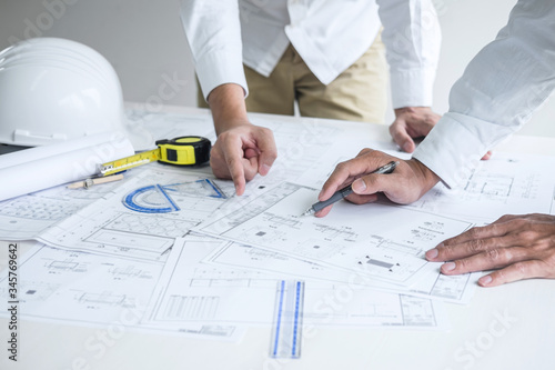 Construction engineering or architect discussing a blueprint and building model while checking information on sketching meeting for architectural project in work site