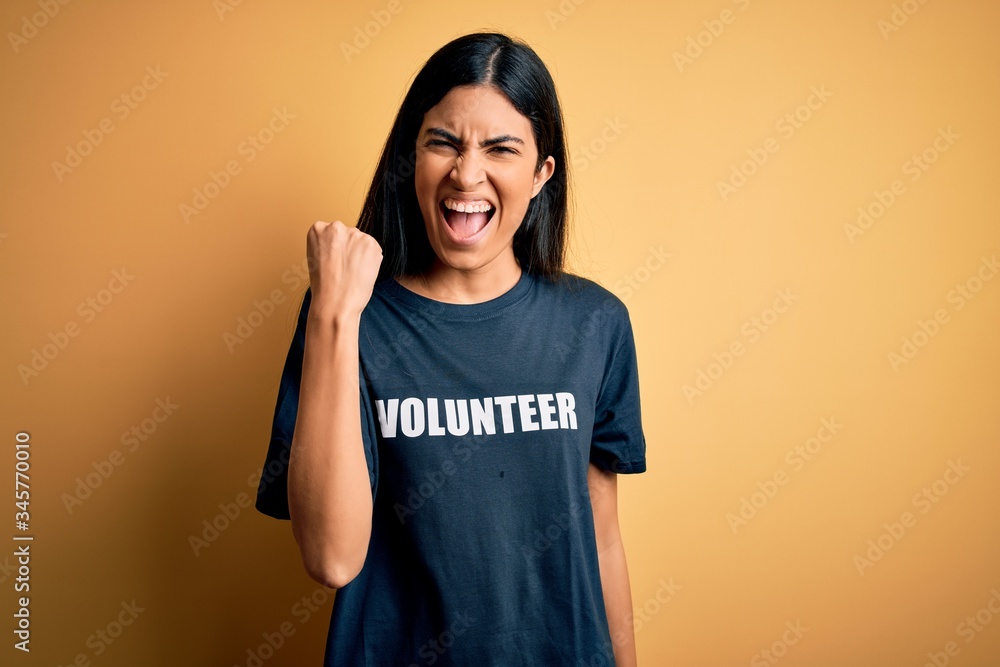 Young beautiful hispanic woman wearing volunteer t-shirt as social charity moral angry and mad raising fist frustrated and furious while shouting with anger. Rage and aggressive concept. Young beautiful hispanic woman wearing volunteer t-shirt as social charity moral angry and mad raising fist frustrated and furious while shouting with anger. Rage and aggressive concept.