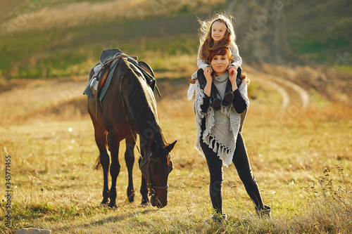 Mother and daughter next to horse. Little girl in a summer field. Family playing with a horse