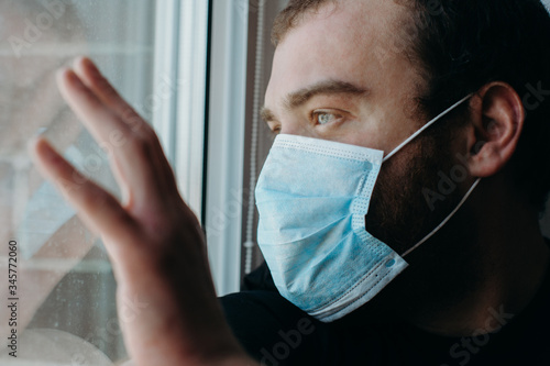 Coronavirus. Sick man of corona virus looking through the window and wearing mask protection.