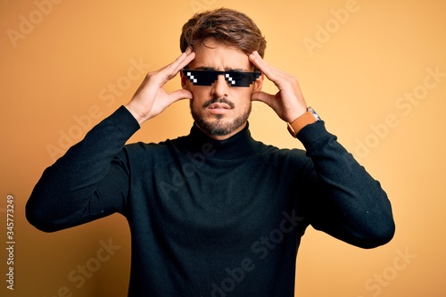 Young man wearing thug life fanny sunglasses standing over isolated yellow background suffering from headache desperate and stressed because pain and migraine. Hands on head. © Krakenimages.com