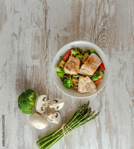 Bol de salmón salvaje, arroz, esparragos trigueros, brócoli, pimiento rojo, champiñones sobre mesa blanco. 