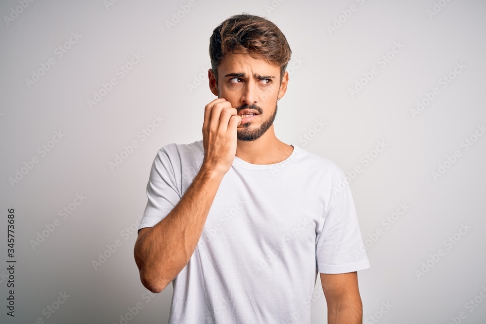 Young handsome man with beard wearing casual t-shirt standing over white background looking stressed and nervous with hands on mouth biting nails. Anxiety problem. Young handsome man with beard wearing casual t-shirt standing over white background looking stressed and nervous with hands on mouth biting nails. Anxiety problem.