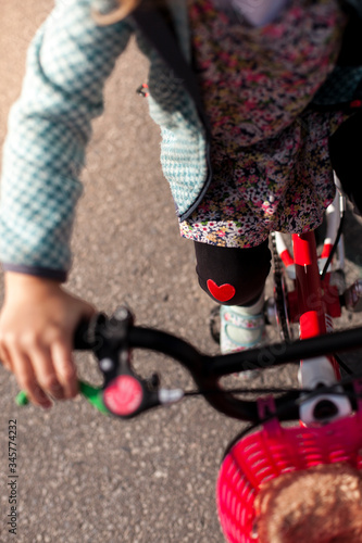 Cute child girl on Bicycle with hurting knee and heart sticker. Healing effect. Junges Mädchen auf Fahrrad mit verletztem Knie und Herz Aufkleber auf Hose. Heilende Wirkung.