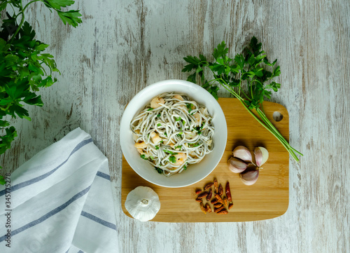 Bol blanco de gulas con gambas, ajos, perejil, guindillas sobre mesa blanca, cenital