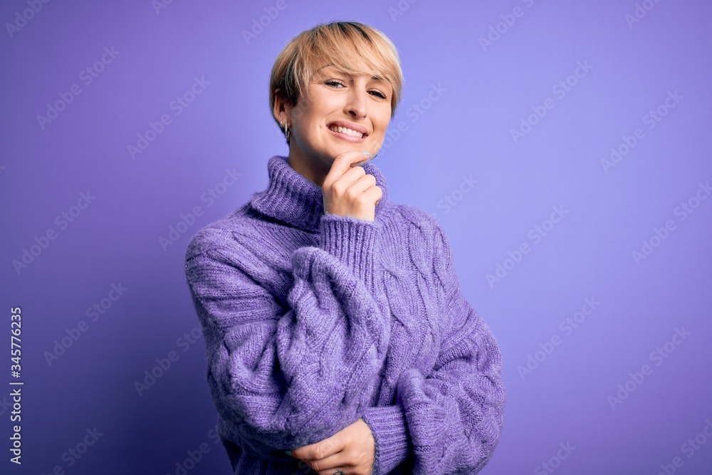 Young blonde woman with short hair wearing winter turtleneck sweater over purple background looking confident at the camera smiling with crossed arms and hand raised on chin. Thinking positive. Young blonde woman with short hair wearing winter turtleneck sweater over purple background looking confident at the camera smiling with crossed arms and hand raised on chin. Thinking positive.