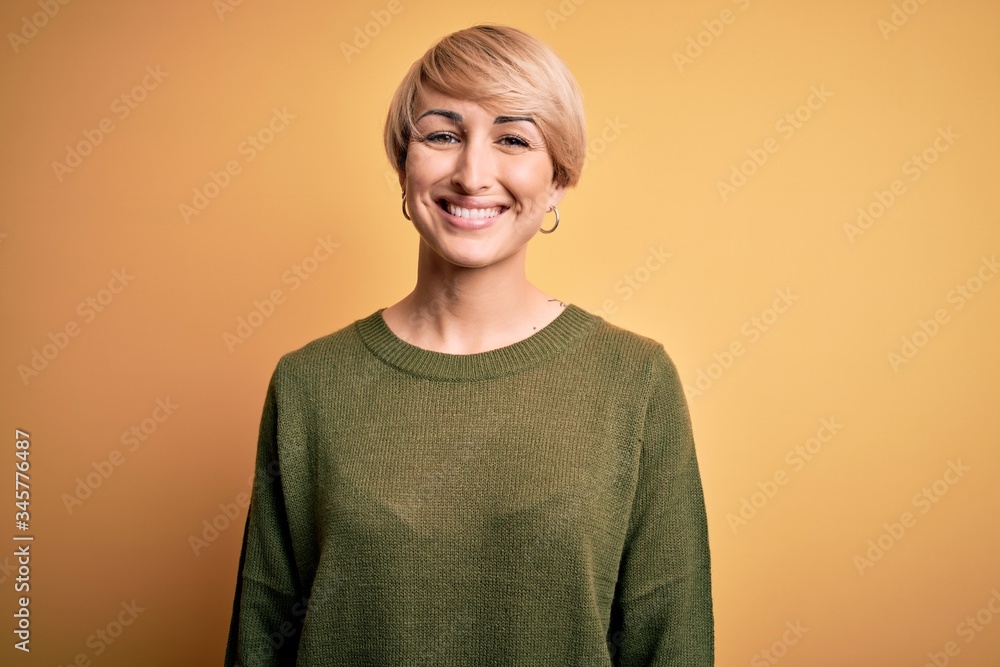 Young blonde woman with modern short hair wearing casual sweater over yellow background with a happy and cool smile on face. Lucky person. Young blonde woman with modern short hair wearing casual sweater over yellow background with a happy and cool smile on face. Lucky person.
