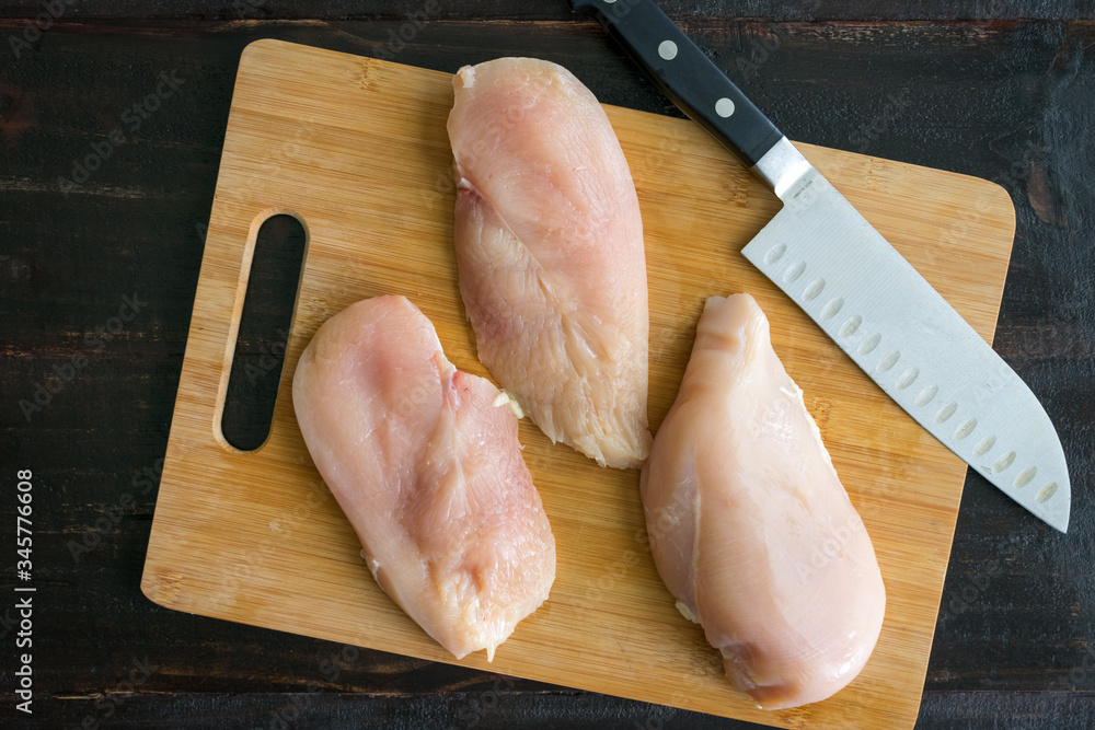 Raw Chicken Cutlets on a Cutting Board: Cutting chicken breasts into cutlets  on a bamboo cutting board Stock Photo