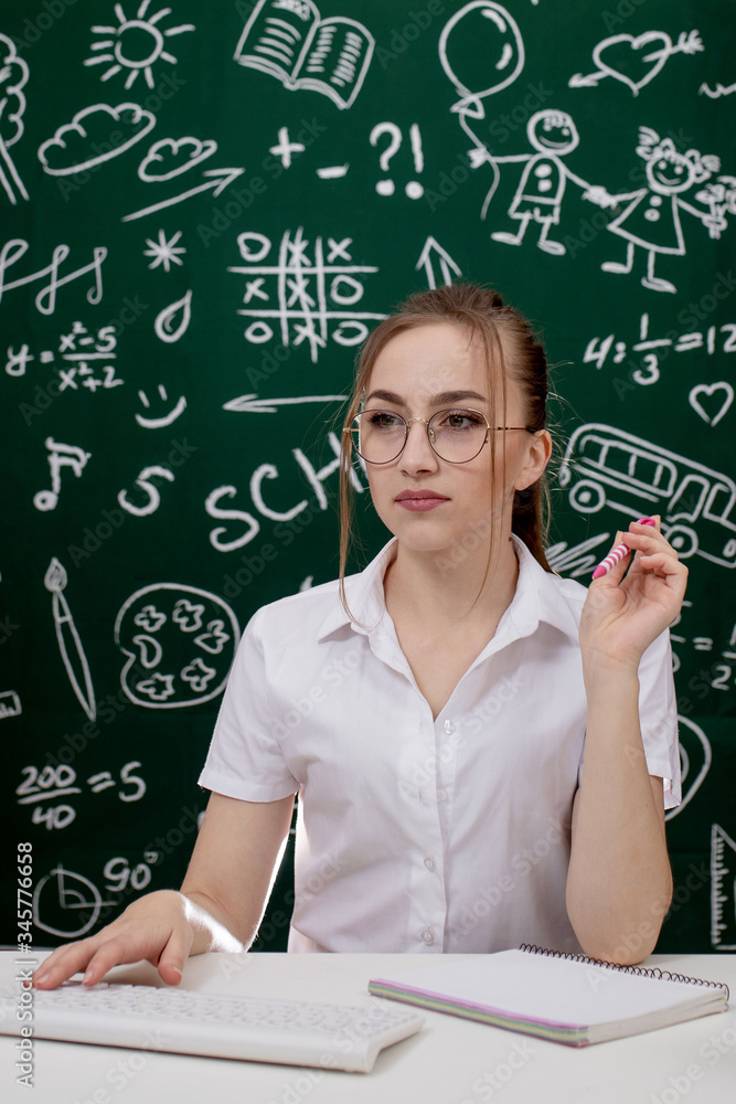 Young teacher is sitting near blackboard in classroom Young teacher is sitting near blackboard in classroom