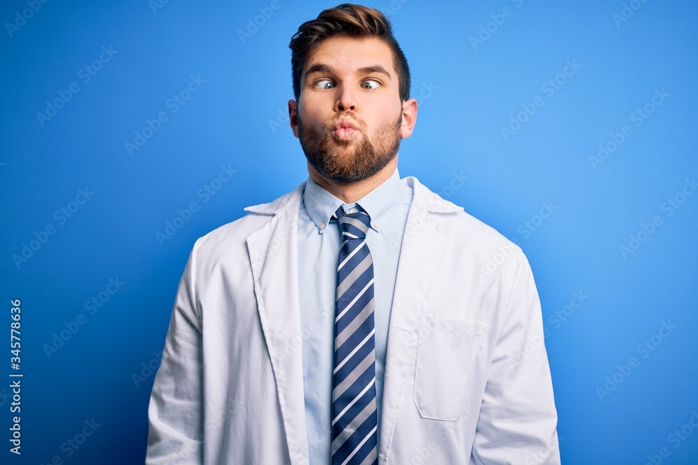 Young blond therapist man with beard and blue eyes wearing coat and tie over background making fish face with lips, crazy and comical gesture. Funny expression. Young blond therapist man with beard and blue eyes wearing coat and tie over background making fish face with lips, crazy and comical gesture. Funny expression.