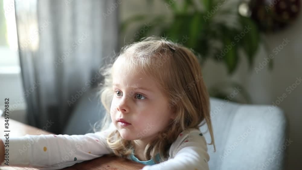 A beautiful little girl with white hair sits at the table and looks closely A beautiful little girl with white hair sits at the table and looks closely