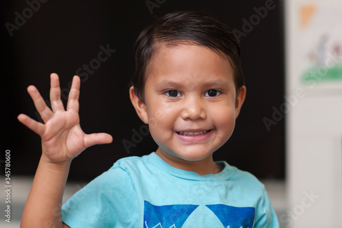 A four year old boy using his fingers to gesture couting to number five  and smiling.