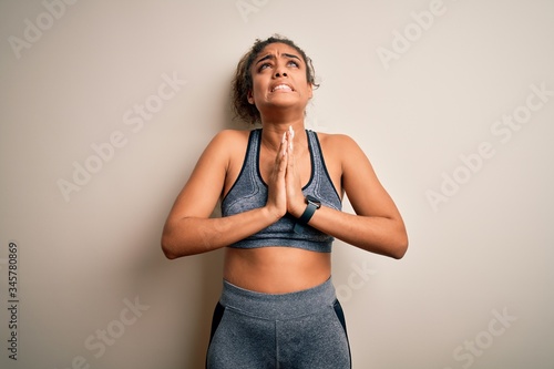 Young african american sportswoman doing sport wearing sportswear over white background begging and praying with hands together with hope expression on face very emotional and worried. Begging.