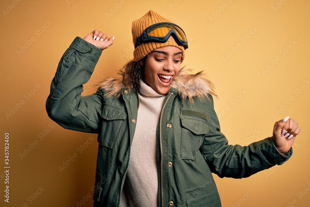 Young african american afro skier girl wearing snow sportswear and ski goggles Dancing happy and cheerful, smiling moving casual and confident listening to music