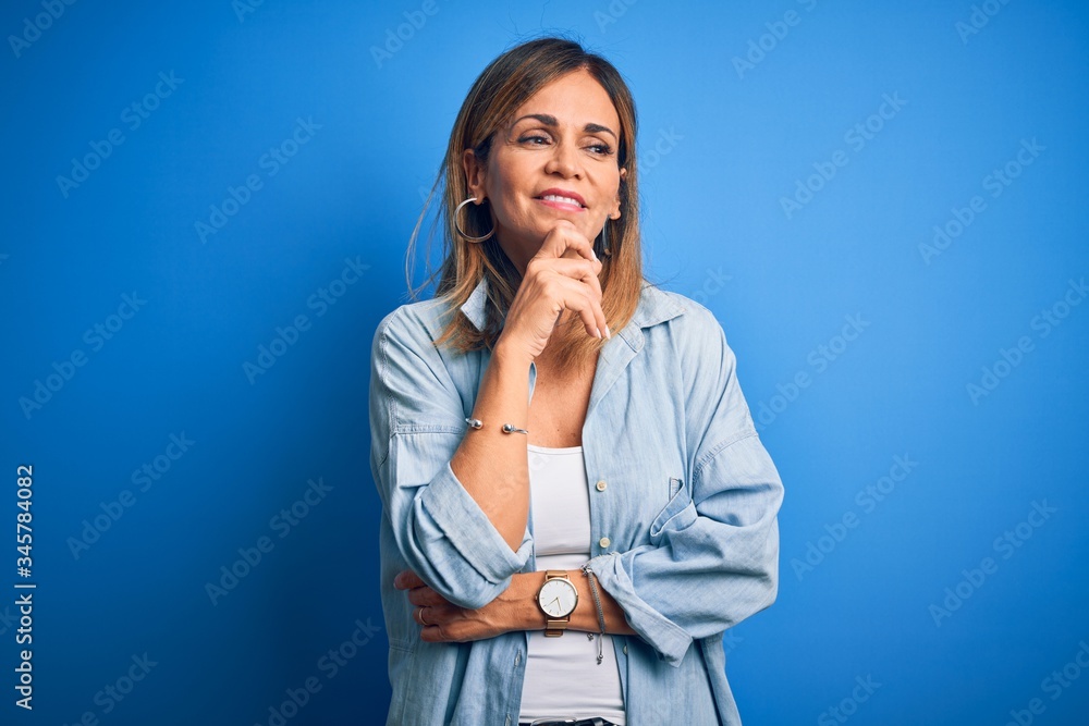Middle age beautiful woman wearing casual shirt standing over isolated blue background with hand on chin thinking about question, pensive expression. Smiling with thoughtful face. Doubt concept. Middle age beautiful woman wearing casual shirt standing over isolated blue background with hand on chin thinking about question, pensive expression. Smiling with thoughtful face. Doubt concept.