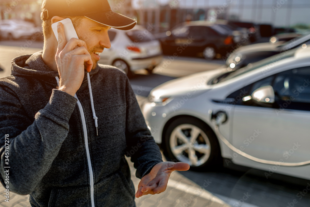 A man waits while his electric car is charging on a charge in a parking lot near a shopping center.