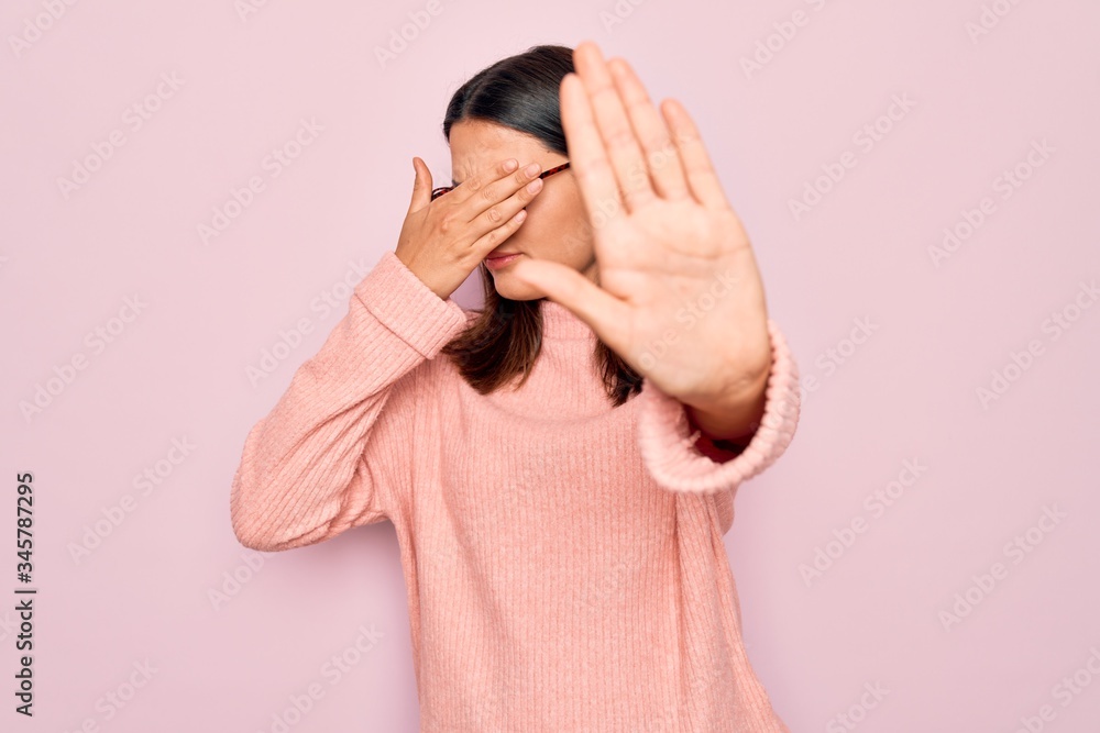 Young beautiful brunette woman wearing casual sweater and glasses over pink background covering eyes with hands and doing stop gesture with sad and fear expression. Embarrassed and negative concept. Young beautiful brunette woman wearing casual sweater and glasses over pink background covering eyes with hands and doing stop gesture with sad and fear expression. Embarrassed and negative concept.