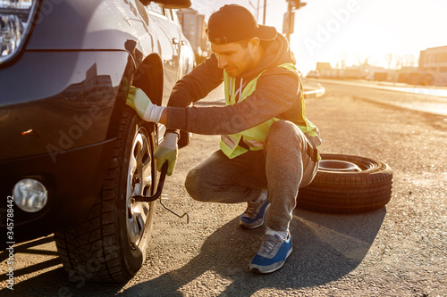 Worker changes a broken wheel of a car. The driver should replace the old wheel with a spare. Man changing wheel after a car breakdown. Transportation, traveling concept