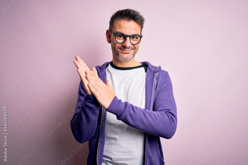 Young handsome man wearing purple sweatshirt and glasses standing over pink background clapping and applauding happy and joyful, smiling proud hands together Young handsome man wearing purple sweatshirt and glasses standing over pink background clapping and applauding happy and joyful, smiling proud hands together