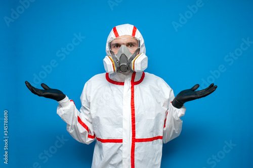 disinfector man in a protective suit shrugs on a blue isolated background, disinfection service worker, coronavirus concept