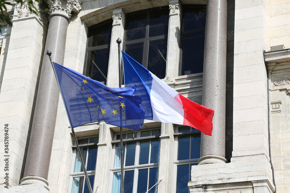 Flag of France and the flag of the European Union are next to the window of a house in the city of Lyon in France.
