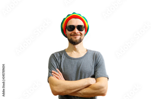 Young caucasian smiling man in rasta hat, sunglasses and grey t-shirt on white background laughing and having fun. photo