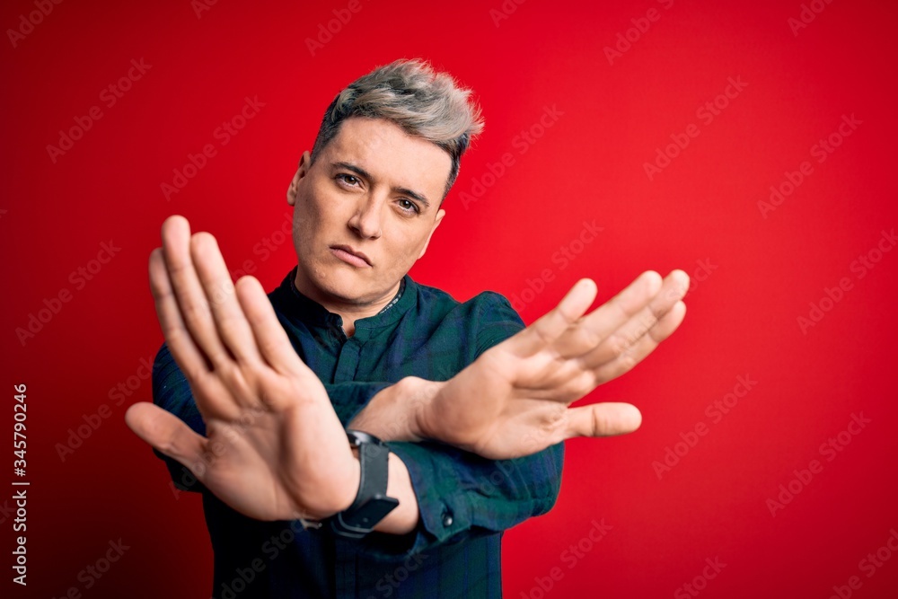 Young handsome modern man wearing elegant green shirt over red isolated background Rejection expression crossing arms and palms doing negative sign, angry face
